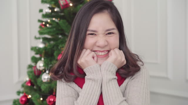 Fröhliche-glücklich-junge-asiatische-Frau-lächelnd-an-Kamera-in-ihrem-Wohnzimmer-zu-Hause-in-Christmas-Festival.-Lifestyle-Frau-feiern-Weihnachten-und-Neujahr-Konzept.