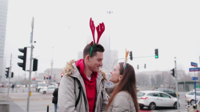 Lovely-Couple-standing-on-the-street-and-wear-Christmas-horns-on-head.-Smile-to-camera-and-give-a-hug