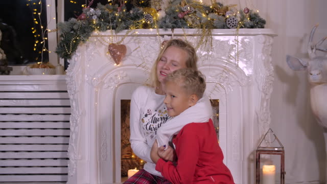 Lächelnde-Schwester-umarmt-Brüderlein-auf-Weihnachten-Kamin-Hintergrund