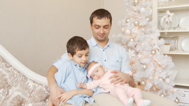 Padre-joven-con-hijo-y-recién-nacido-en-un-sofá-en-Navidad