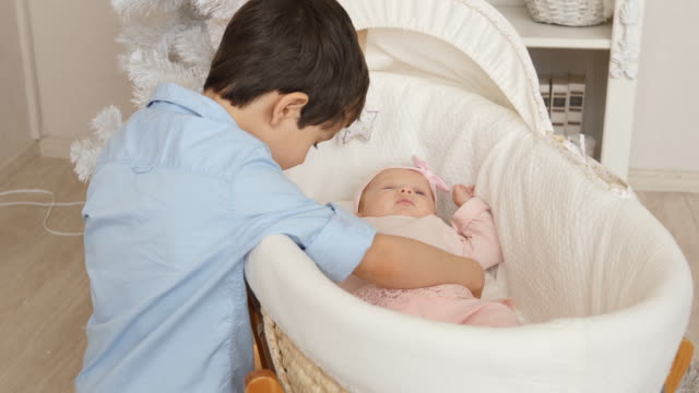 Little-brother-swings-at-bed-with-her-newborn-sister