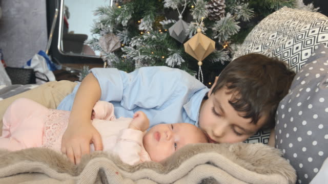 Little-brother-and-newborn-sister-lie-on-a-bed-in-Christmas