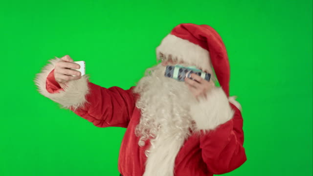 Weihnachtsmann-mit-einem-großen-Geschenk,-das-ein-Selfie-auf-dem-Smartphone-auf-einem-Green-Screen-Chrome-Key-macht