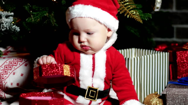 bebé-traje-de-Santa,-Santa-Claus-poco-muchacho,-niño-se-sienta-en-los-trajes-de-carnaval,-trajes-de-la-Navidad-bajo-el-árbol-de-Navidad