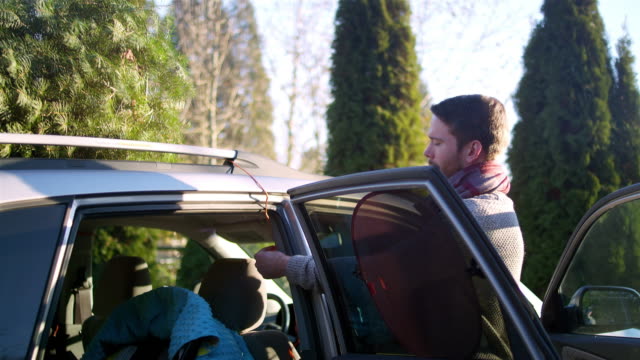 Young-man-tying-a-Christmas-tree-to-the-car-with-rope