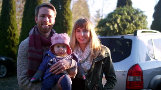 Retrato-de-una-joven-madre,-padre-y-bebé-delante-de-su-coche-con-árbol-de-Navidad-en-la-parte-superior