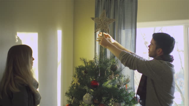 Young-man-puts-a-star-ornament-on-the-top-of-the-Christmas-tree