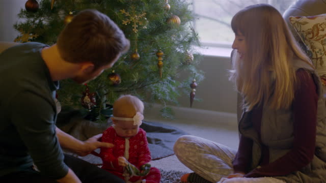 Parents-opening-presents-with-their-baby-in-front-of-the-tree-on-Christmas-morning