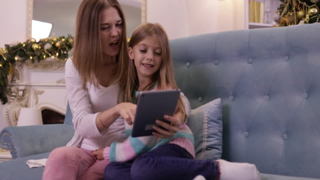 Mutter-mit-Tochter-auf-Couch-mit-Tablet-Computer-Happy-Smiling-junge-Familie-in-der-Nähe-dekorierten-neuen-Jahr-Weihnachtsbaum