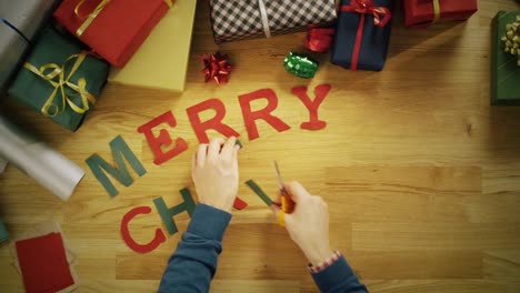 Vista-superior-Time-lapse-de-un-corte-de-hombre-de-letras-para-las-palabras-\"Feliz-Navidad\"-y-lLaying-les-en-la-mesa-con-regalo-envuelto-cajas-de-madera.