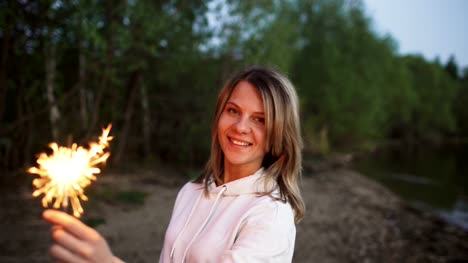 Portrait-of-young-smiling-woman-with-sparkler-celebrating-at-beach-party