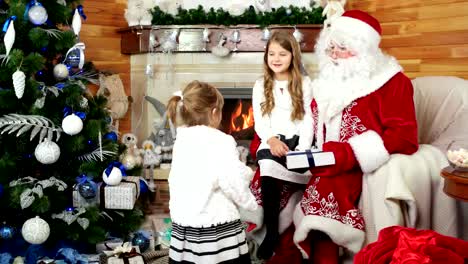 kleine-Mädchen-besuchen-Santa-in-seiner-Residenz,-glückliche-Schwester-auf-Santa-Claus-Schoß,-Weihnachtsgeschenke