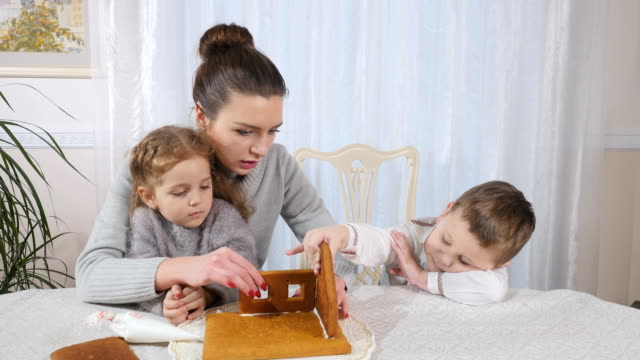 Junge-Mutter-mit-Kindern-macht-ein-Lebkuchenhaus-in-der-Küche