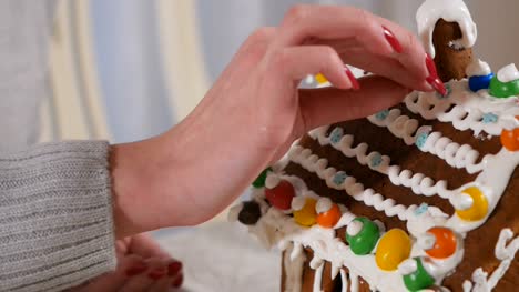 Female's-hand-puts-a-small-snowflakes-on-sweet-cream-on-gingerbread-house