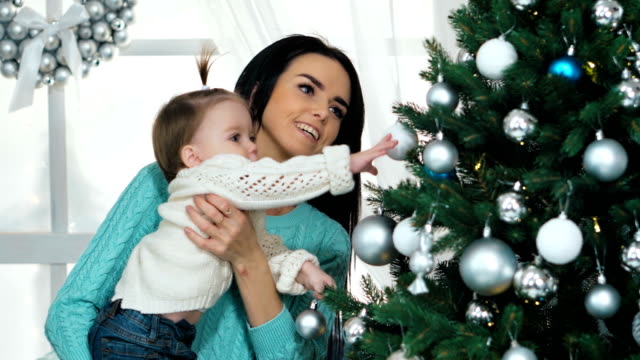 Mutter-mit-ihren-10-Monate-alten-Baby-Girl-dekorieren-Weihnachtsbaum-im-Wohnzimmer