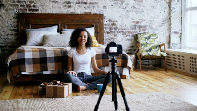 Young-cheerful-mixed-race-girl-recording-video-blog-about-packing-christmas-gift-box-at-home