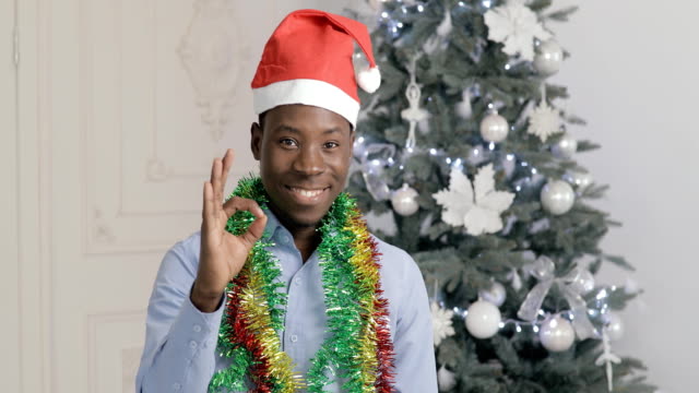 Okay-and-thumbs-up-gesture-of-african-man-in-Santa-Claus-hat,-Christmas-holiday