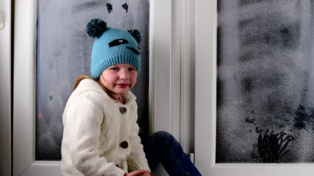 Small-girl-sits-on-windowsill-behind-the-frozen-window.