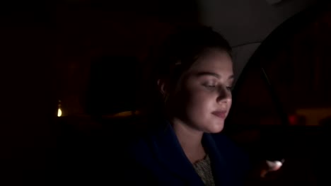 Happy-smiling-girl-riding-in-a-taxi-at-night-sitting-on-the-backseat-and-texting-using-her-smartphone.-Happy-woman-in-taxi.-Night-live.-Slowmotion-shot
