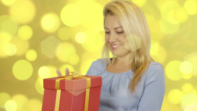 Glückliche-kaukasische-Frauen-nehmen-rote-Geschenkbox-auf-Goldgrund.-Lächelnde-Frau.-Überraschung-zu-präsentieren.