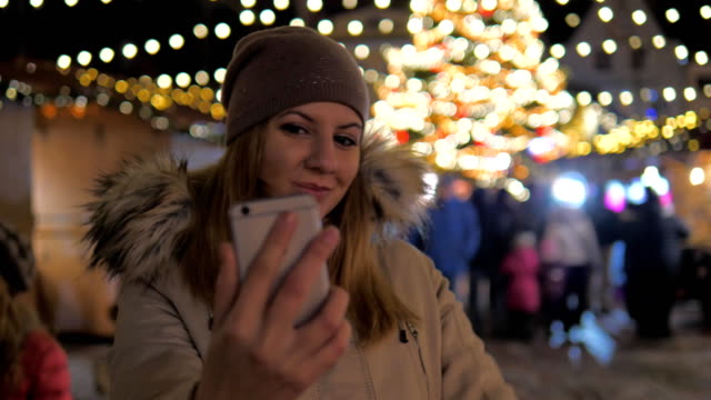 Joven-sonriente-mujer-Selfie,-permanente-en-el-mercado-de-Navidad-con-iluminaciones