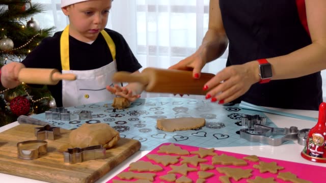 The-little-kid-boy-helps-mother-to-cook-Christmas-ginger-biscuit-in-light-kitchen.-Happy-family-mom-30-35-years-and-child-3-4-roll-out-dough-and-cut-out-cookies-at-home.-Relationship-and-love-concept