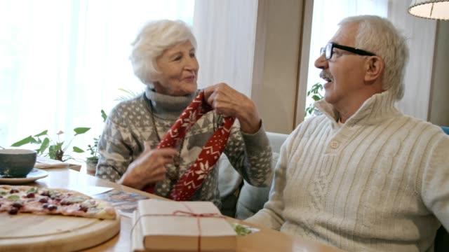 Elderly-Woman-Putting-Scarf-on-Man-at-Christmas-Dinner-in-Cafe