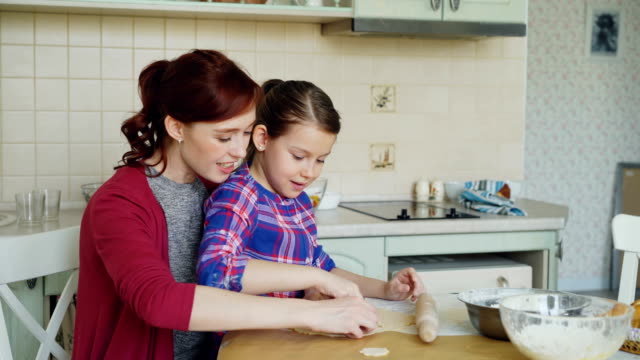 Smiling-mother-and-cute-daughter-making-cookies-together-using-bakery-forms-while-sitting-in-modern-kitchen-at-home.-Family,-food-and-people-concept