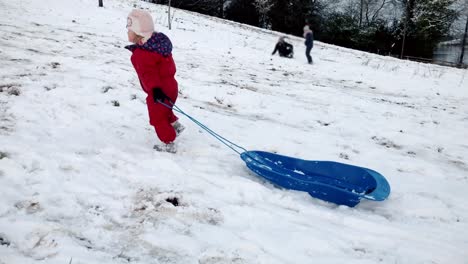 Junge-kleinkind-mädchen-Ziehen-eines-Schlittens-auf-einem-schneebedeckten-Hügel