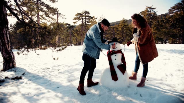Joven-pareja-haciendo-muñeco-de-nieve-en-el-bosque-de-montaña-cubierto-de-nieve