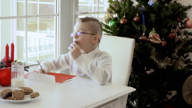 Fröhlicher-junge-schreibt-einen-Brief-an-den-Weihnachtsmann-und-isst-cookies