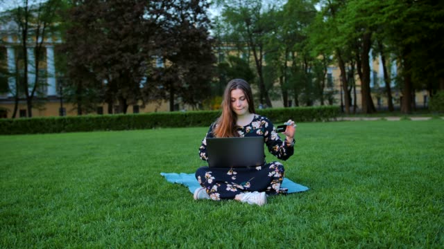 A-female-in-summer-dress-with-a-laptop-and-a-credit-card-outdoors