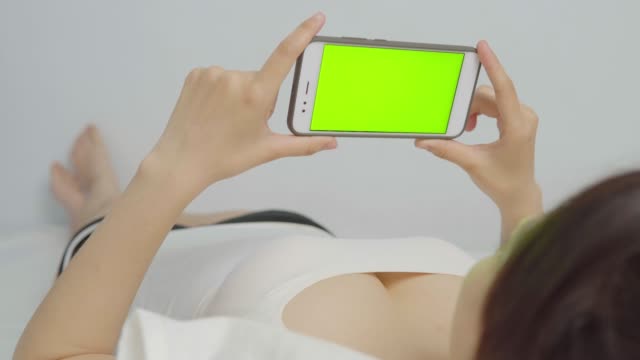 Frau-nehmen-Handy-mit-green-Screen-auf-dem-Bett