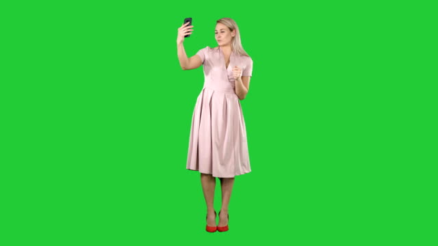 Mature-woman-wearing-light-pink-dress-making-selfie-on-a-Green-Screen,-Chroma-Key