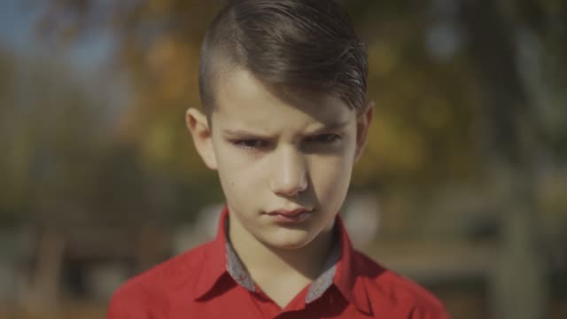 Portrait-of-a-little-boy-looking-at-first-sad-and-then-smiling.-Cute-child-in-a-red-shirt-spends-time-outdoors.-Sadness-and-smile.