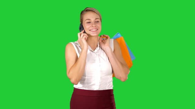 Shopper-woman-calling-with-smart-phone-holding-shopping-bags-and-walking-on-a-Green-Screen,-Chroma-Key