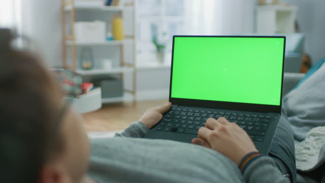 Mann-im-Hause-Verlegung-auf-eine-Couch-mit-grünen-Mock-Up-Screen-Laptop-Computer.-Mann-mit-Laptop-Gerät,-Internet-surfen,-Inhalte,-Videos-anschauen.