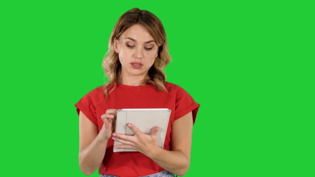 Lady-wearing-red-t-shirt-holding-a-tablet-in-her-hands-with-a-serious-face-talking-to-camera-on-a-Green-Screen,-Chroma-Key