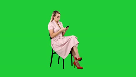 Mujer-joven-con-pelo-rubio-sentado-en-una-silla-de-lectura,-mensajes-de-texto-a-teléfono-celular-en-una-pantalla-verde-Chroma-Key