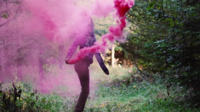 Beautiful-girl-in-a-forest-waves-a-pink-smoke-grenade-around-in-circles,-slow-motion
