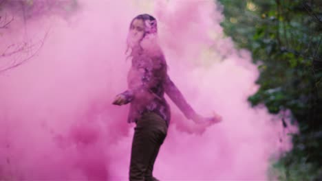 Beautiful-girl-in-a-forest-spins-around-while-holding-a-pink-smoke-grenade,-slow-motion