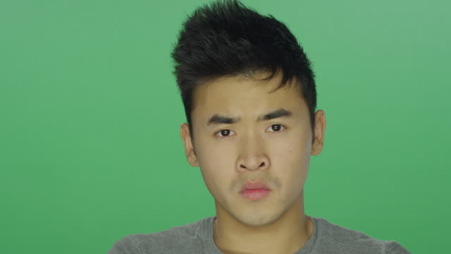 Young-man-crossing-his-arms-and-staring,-on-a-green-screen-studio-background