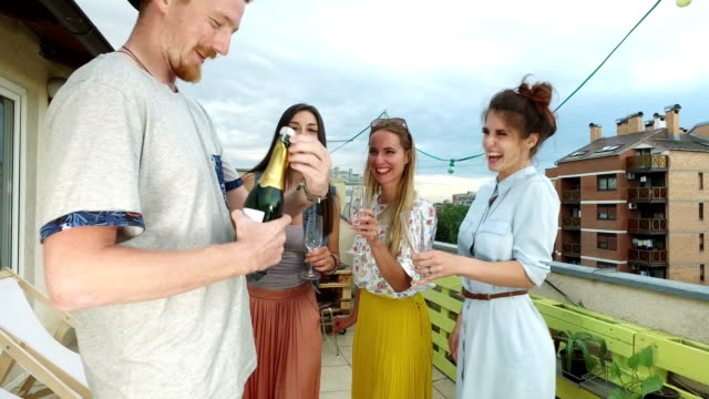 Side-view-of-hipster-man-opening-champagne,-female-friends-waiting-with-glasses