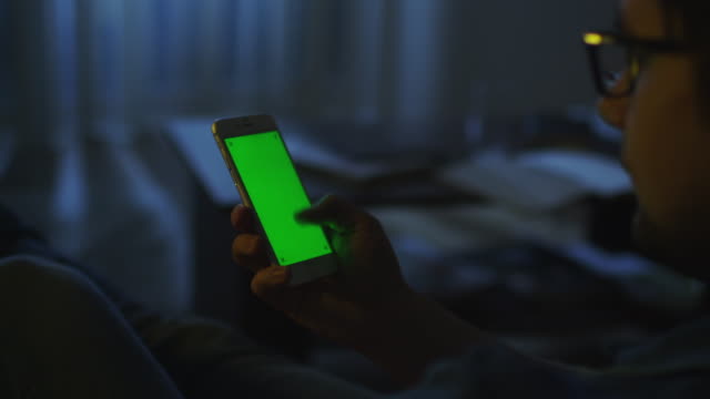 El-hombre-está-acostado-en-el-sofá-por-la-noche-y-usando-el-teléfono-con-la-pantalla-verde-en-el-modo-retrato.