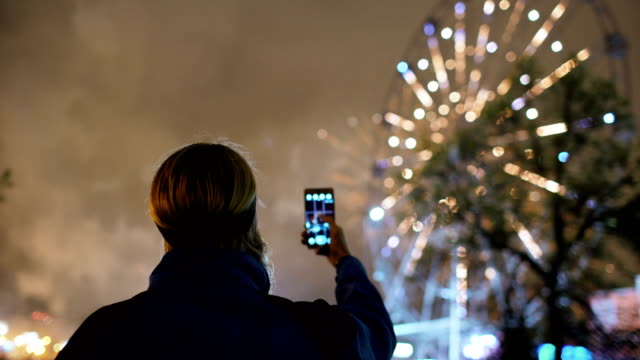 Closeup-silhouette-of-man-watching-and-photographing-fireworks-explode-on-smartphone-camera-outdoors
