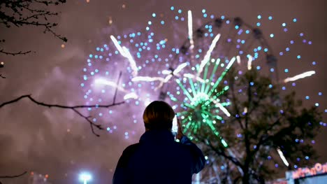 Closeup-silhouette-of-man-watching-and-photographing-fireworks-explode-on-smartphone-camera-outdoors