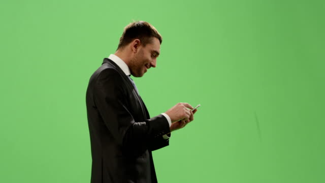Empresario-en-un-traje-utiliza-un-smartphone-mientras-caminaba-por-una-maqueta-pantalla-verde-de-fondo.