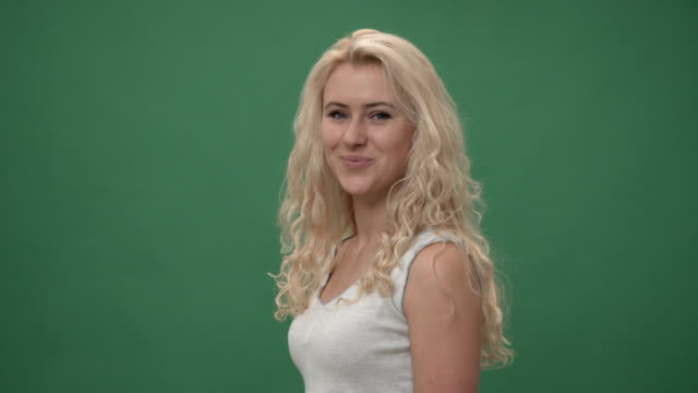 Young-blonde-woman-in-a-white-top-is--turning-to-the-camera-and-smiling,-chroma-key-green-screen-background