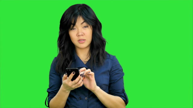 Nachdenklich-asiatische-Geschäftsfrau-lesen-Präsentation-auf-Smartphone,-Blick-in-die-Kamera-auf-einem-Green-Screen,-Chroma-Key