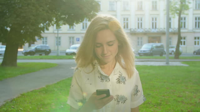 Young-woman-using-smartphone-in-the-city-park-at-sunrise.